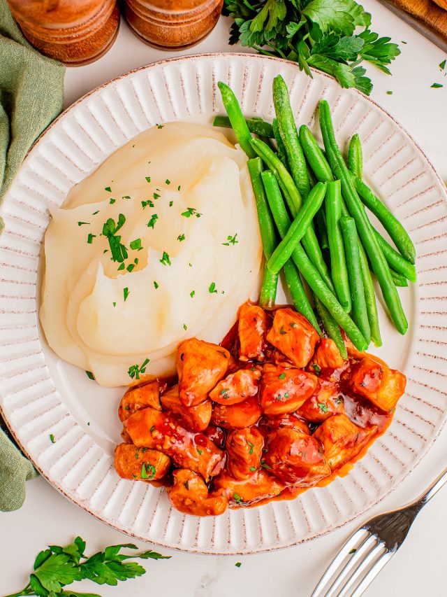 A plate with mashed potatoes, green beans, and barbecue-glazed chicken pieces, garnished with chopped parsley.