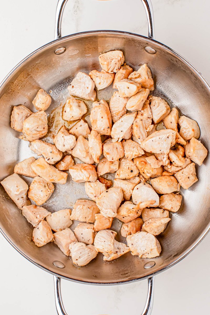 Cooked, cubed pieces of chicken breast in a stainless steel pan on a white background.