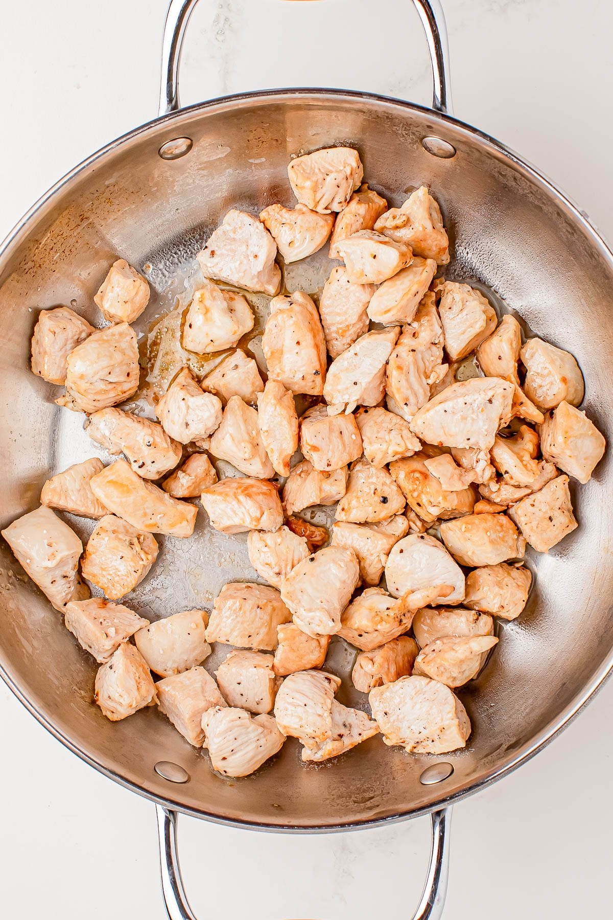Cooked, cubed pieces of chicken breast in a stainless steel pan on a white background.