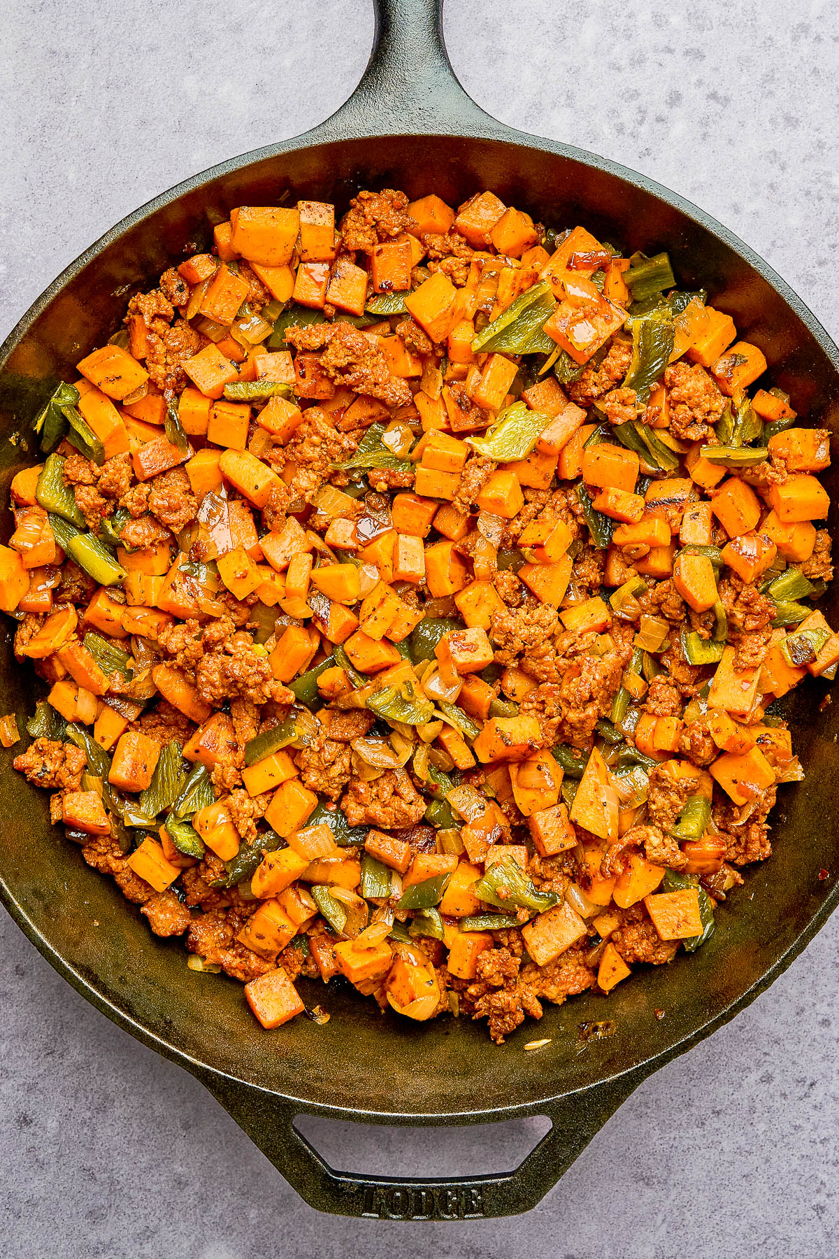 A cast iron skillet filled with a cooked mixture of ground meat, diced sweet potatoes, and chopped green vegetables.
