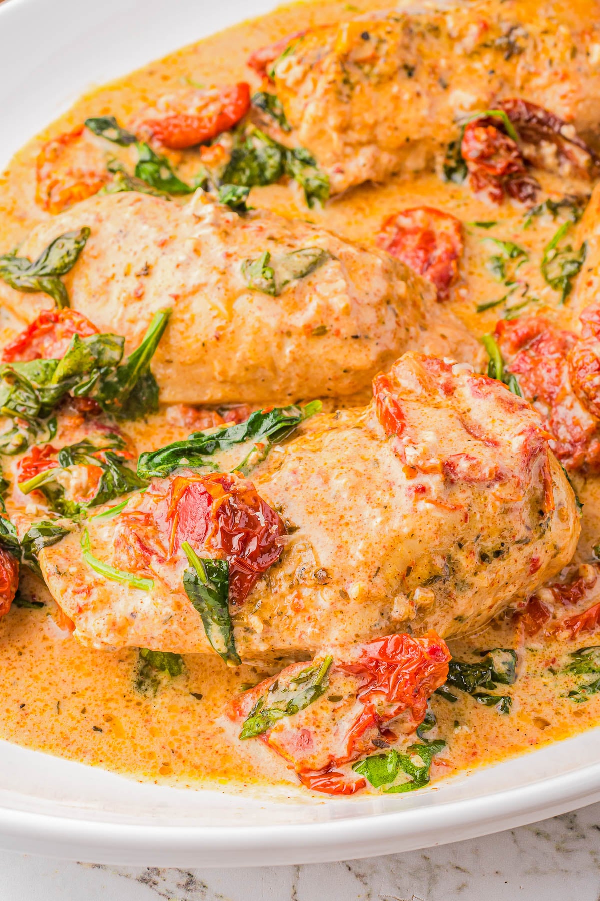 Chicken breasts in a creamy sauce with wilted spinach and sun-dried tomatoes, served in a white dish.