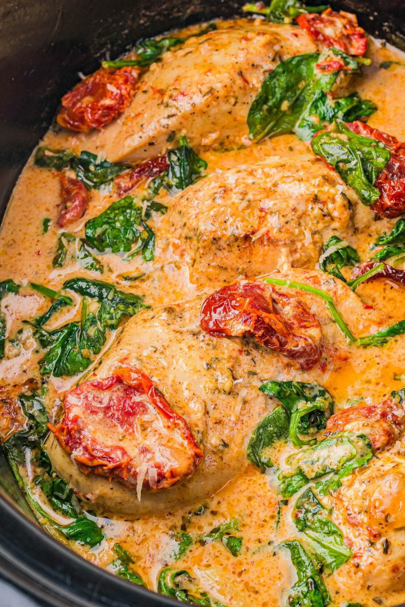 Chicken breasts cooked in a creamy sauce with spinach and sun-dried tomatoes in a slow cooker.