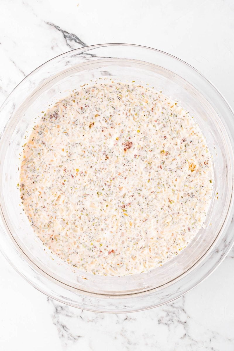 A clear glass bowl filled with a creamy, speckled mixture sitting on a white marble surface.