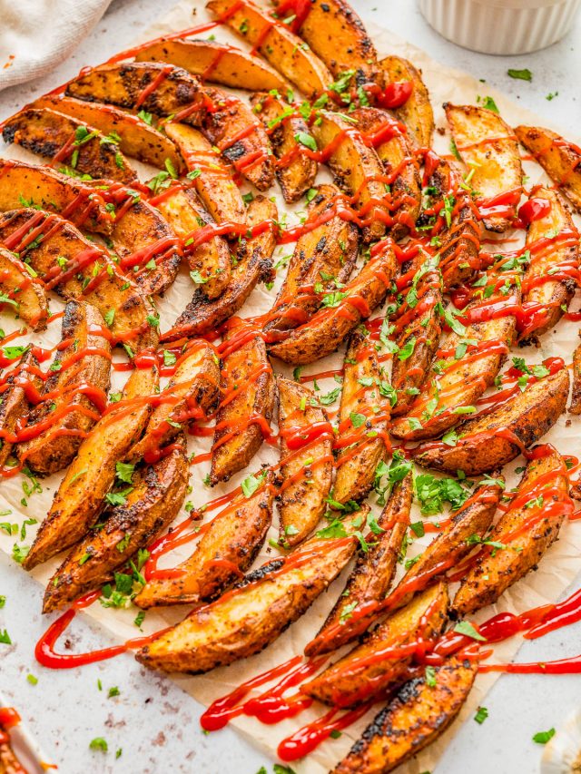 Seasoned potato wedges garnished with chopped herbs and drizzled with ketchup, arranged on parchment paper.