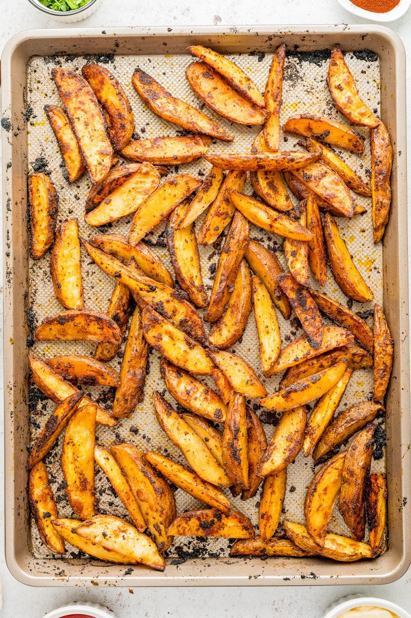A baking sheet filled with seasoned, golden-brown potato wedges on a parchment-lined tray, viewed from above.