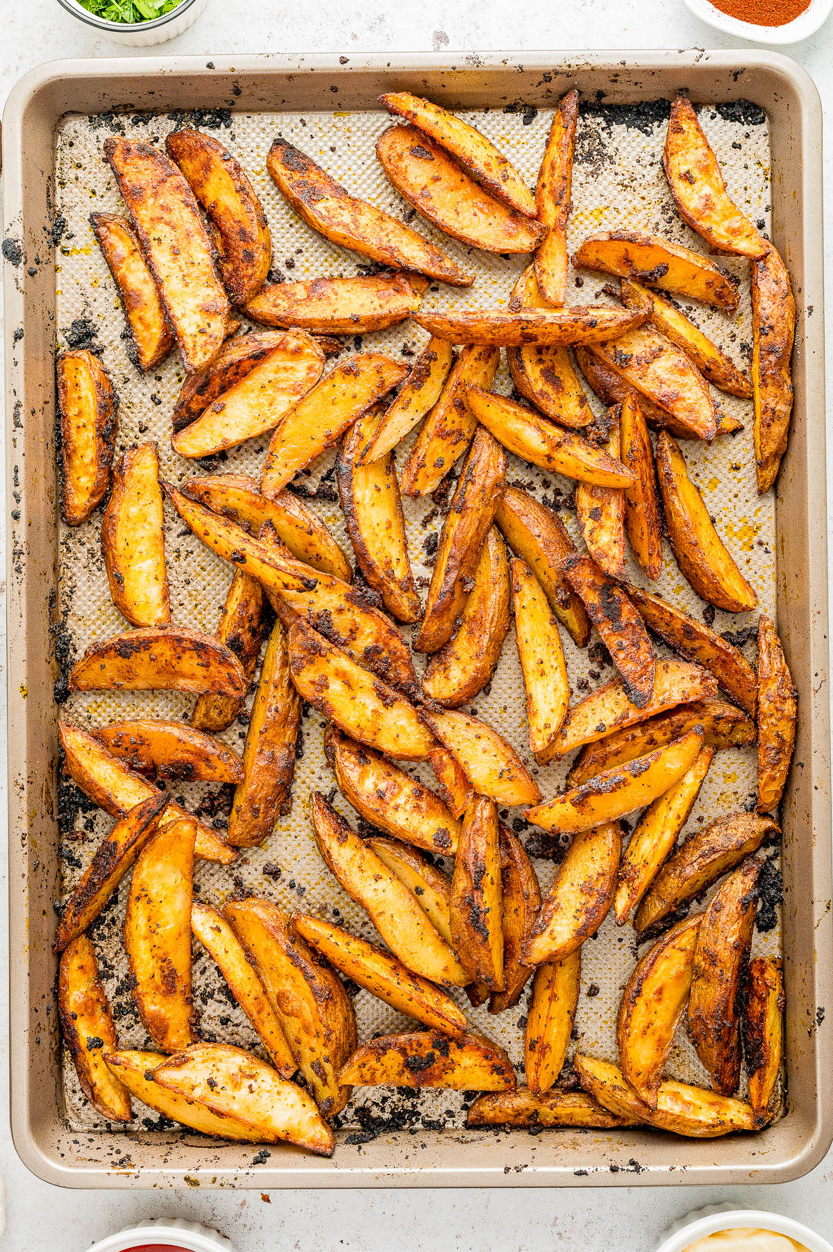 A baking sheet filled with seasoned, golden-brown potato wedges on a parchment-lined tray, viewed from above.