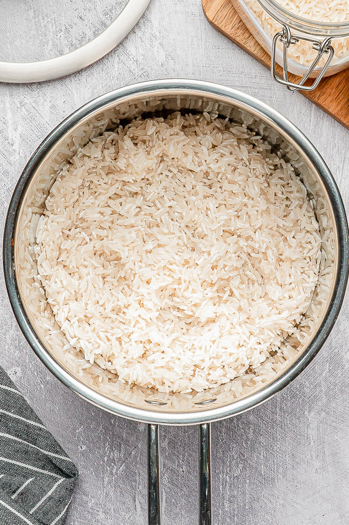 A stainless steel pot filled with uncooked white rice sits on a light gray countertop.