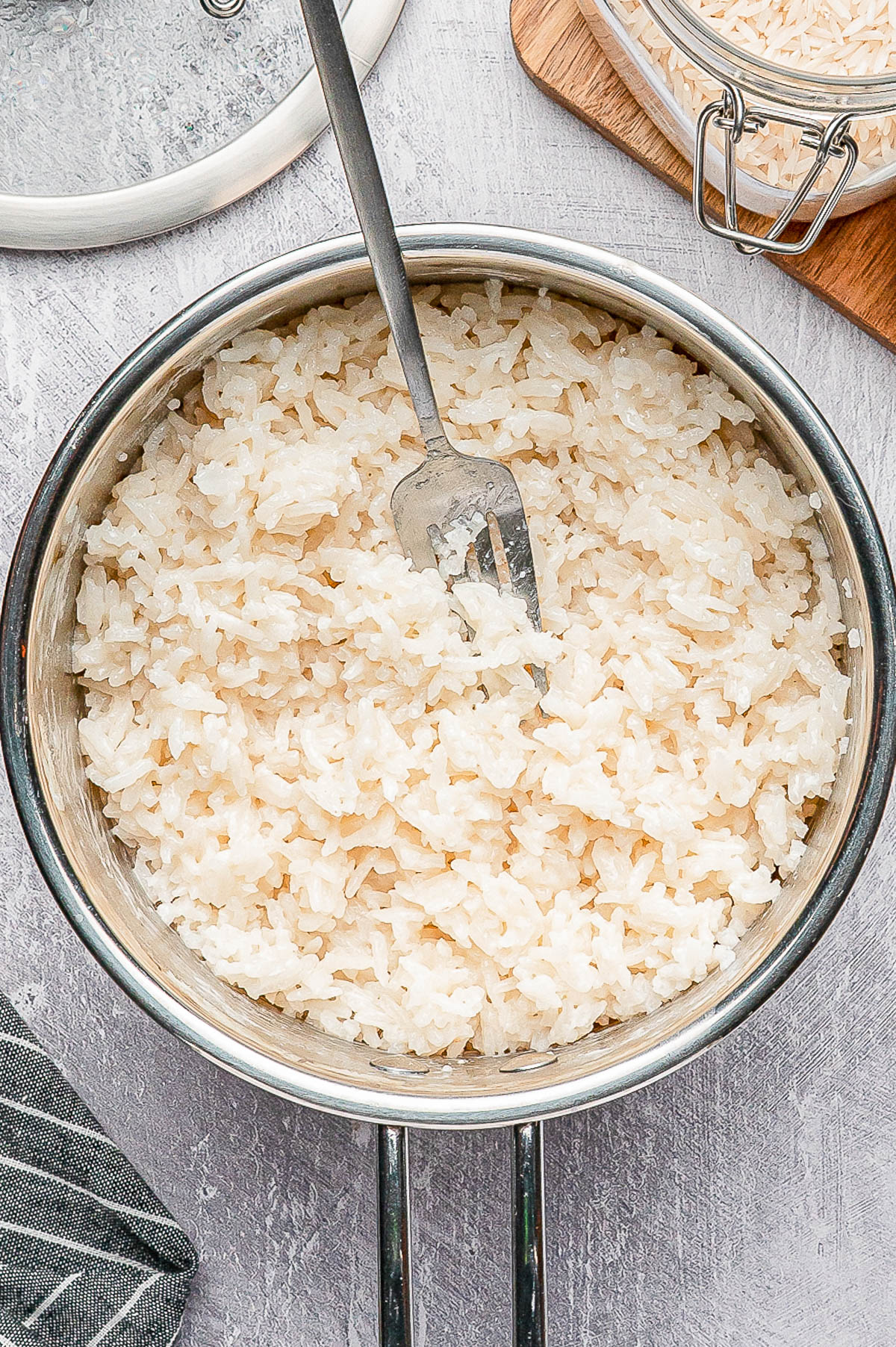 A pot of cooked white rice with a fork inside, placed on a light gray surface.