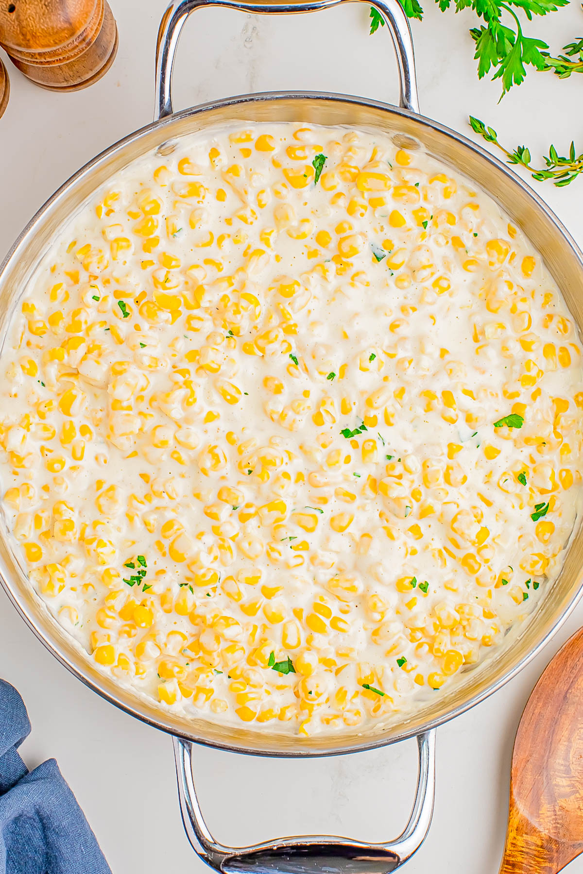 A large skillet filled with creamy corn garnished with small pieces of parsley on a white countertop.