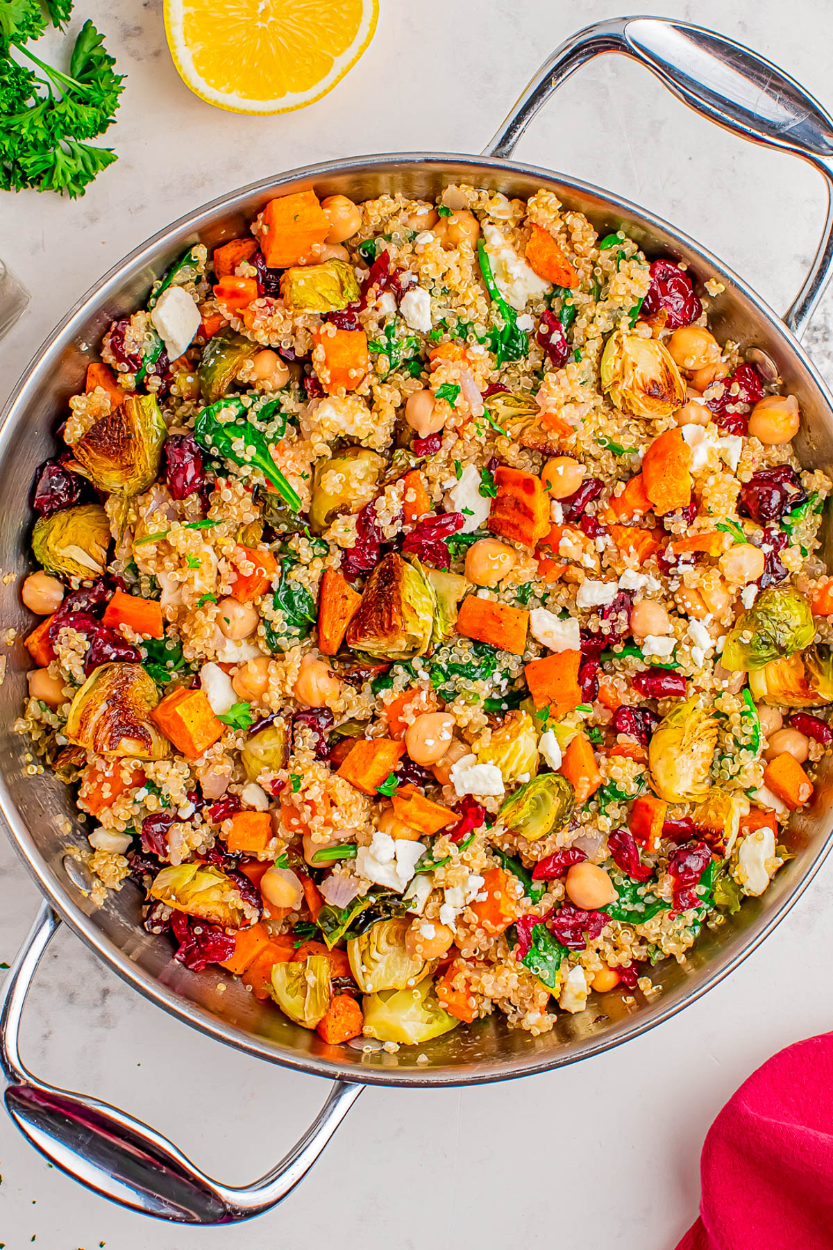 A skillet filled with quinoa, roasted Brussels sprouts, sweet potatoes, chickpeas, spinach, dried cranberries, and crumbled feta cheese on a marble countertop.