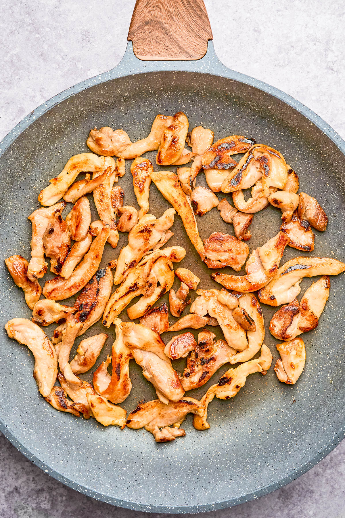 Sliced pieces of cooked chicken breast in a non-stick frying pan on a light surface.