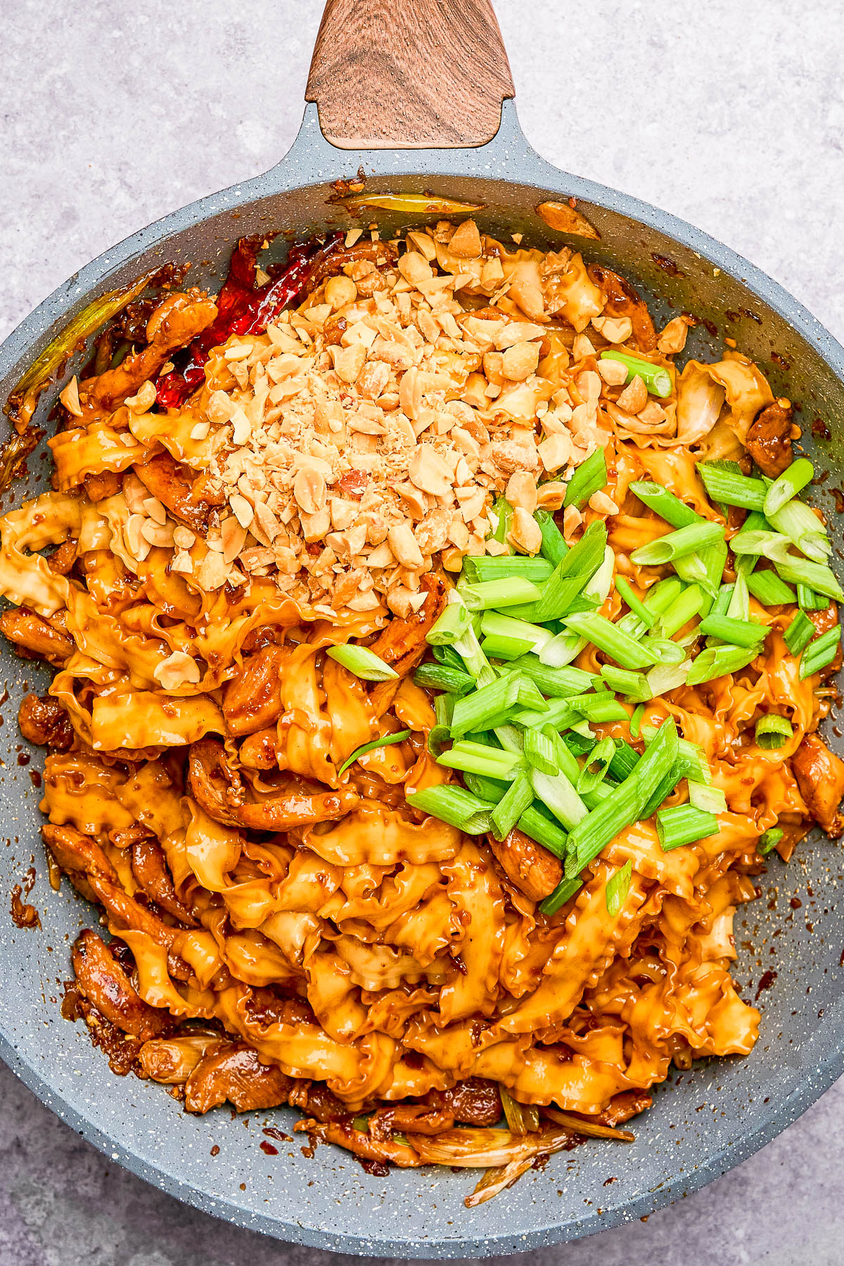 A skillet filled with wide noodles in sauce, topped with chopped peanuts and sliced green onions.