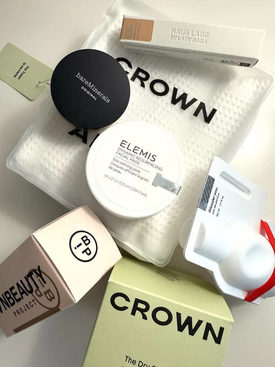 A variety of skincare and beauty products, including brands like Elemis, bareMinerals, Haus Labs, and INNBeauty Project, arranged on a white textured surface.