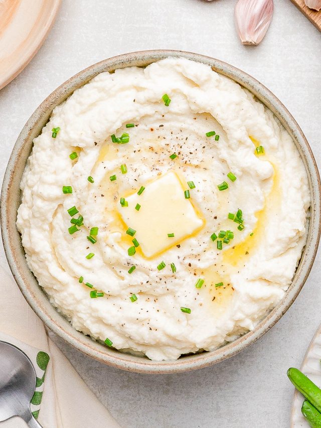 A bowl of mashed potatoes topped with a pat of melting butter, chopped chives, and cracked black pepper.