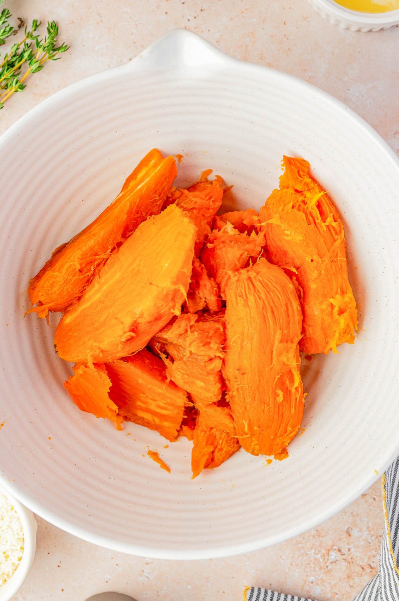 A white bowl containing peeled and cooked sweet potato pieces on a light countertop.