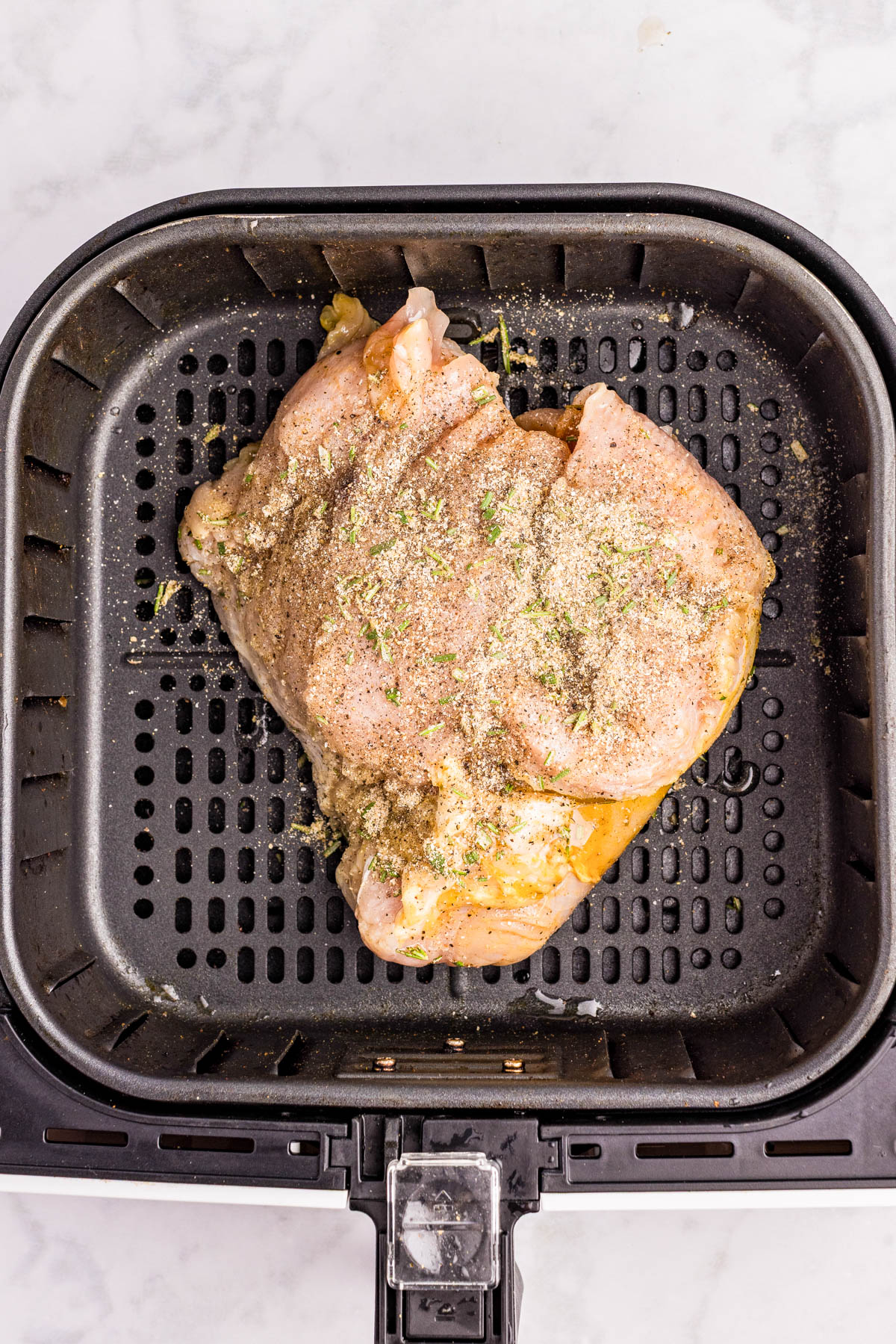 Raw, seasoned chicken breast placed inside an air fryer basket, ready to be cooked.
