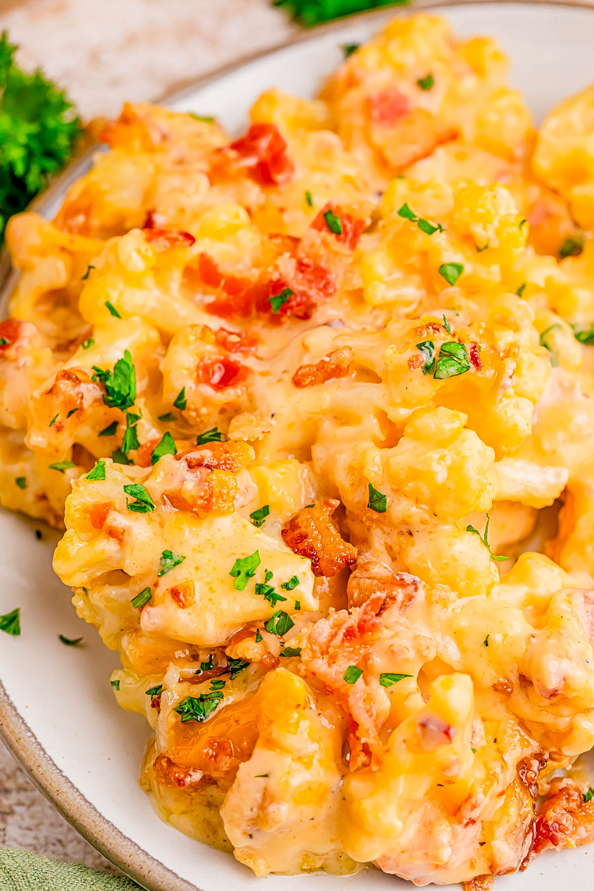 A serving of cheesy cauliflower casserole topped with bacon bits and chopped parsley on a white plate.