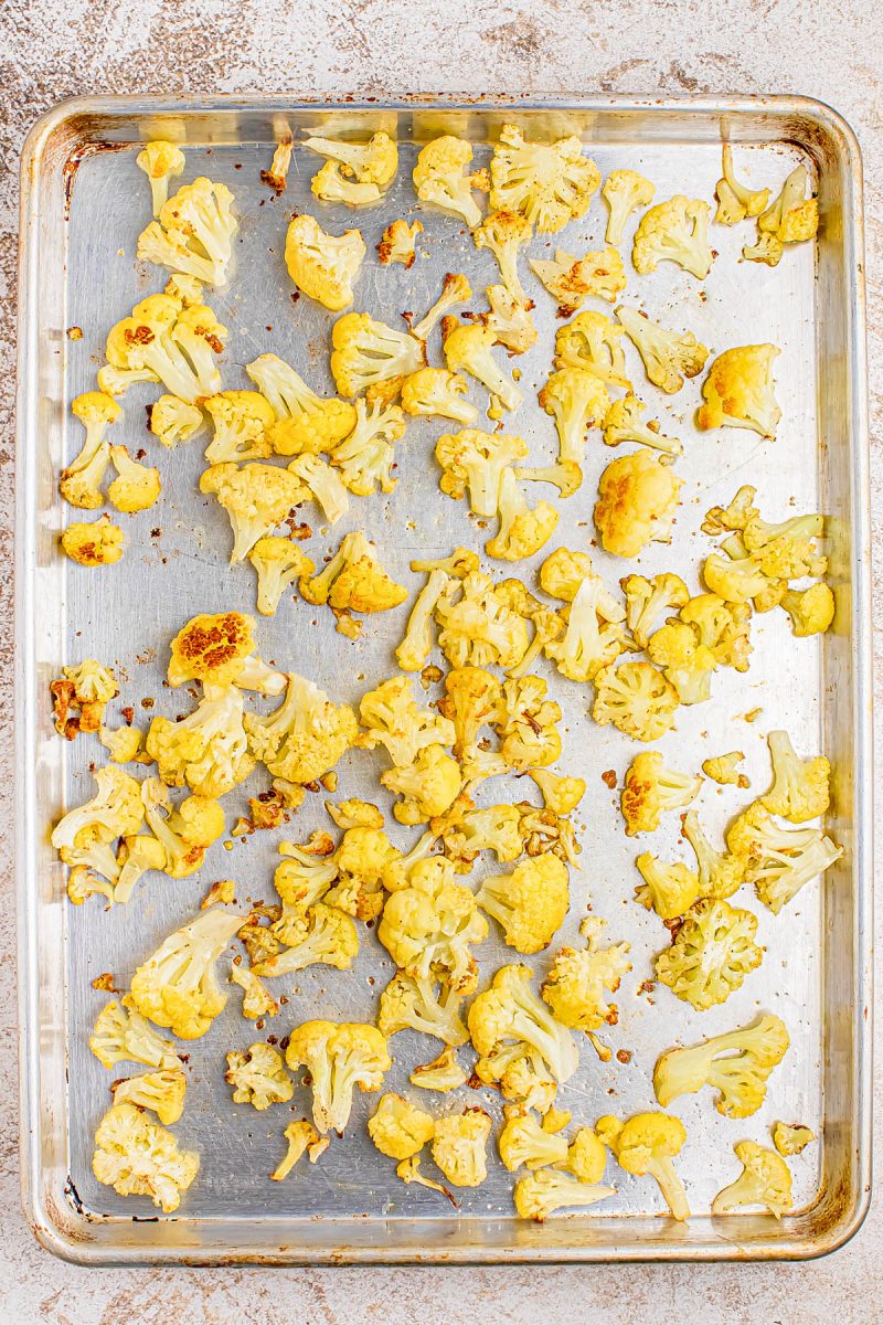 Roasted cauliflower florets spread out on a metal baking sheet, lightly browned in some spots.