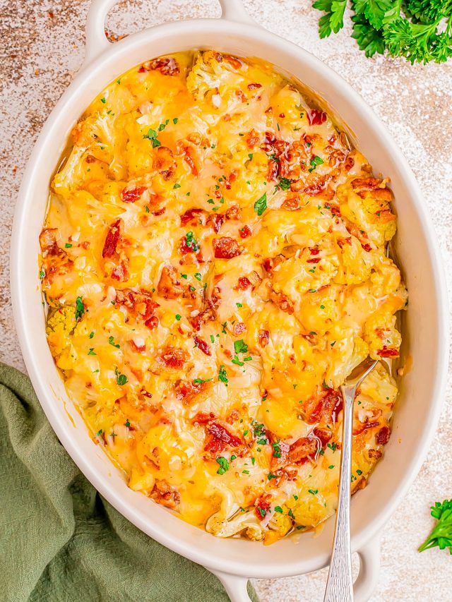A casserole dish filled with cheesy potatoes topped with bacon bits and chopped parsley, with a serving spoon inside.
