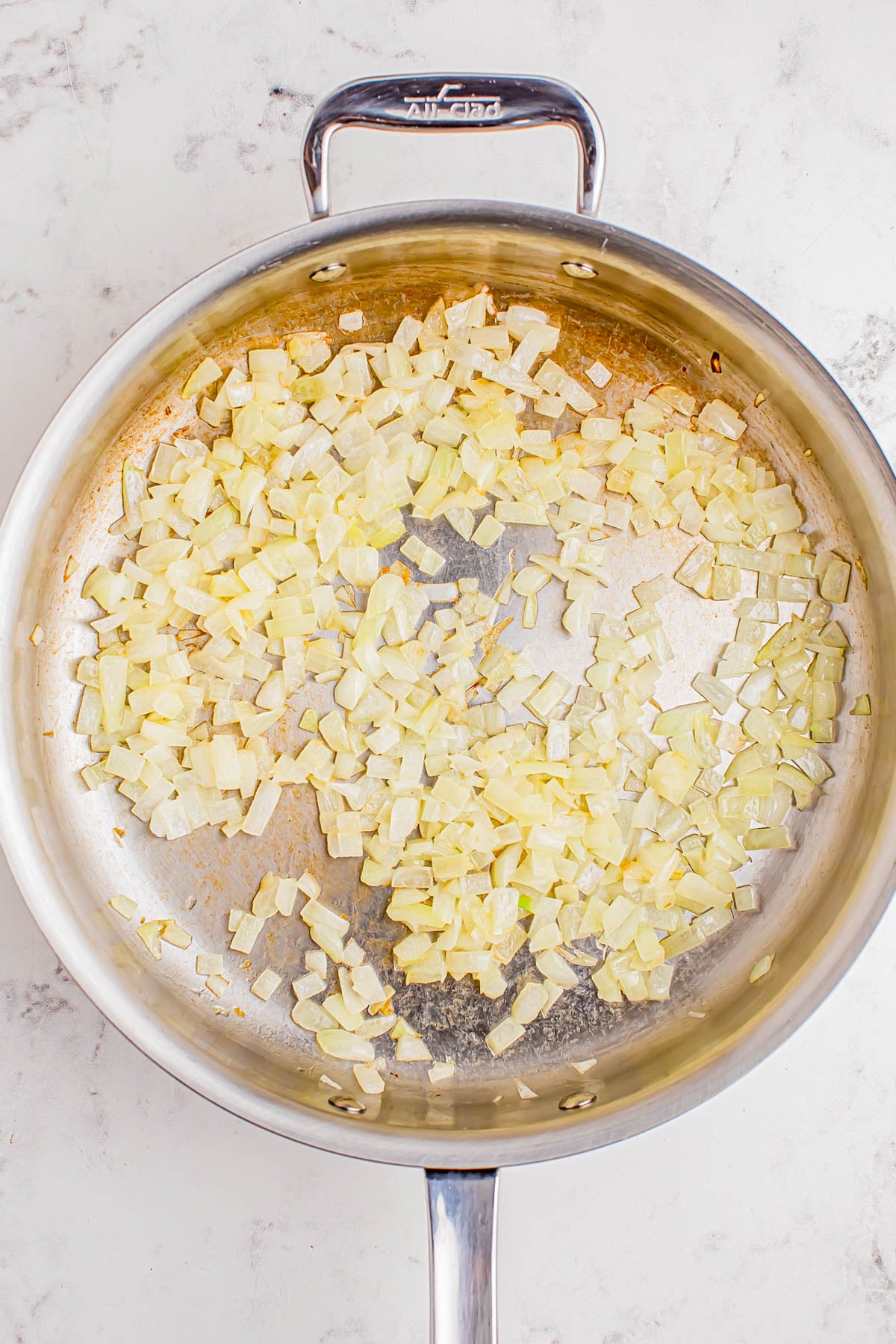 Diced onions sautรฉing in a stainless steel pan on a light-colored surface.