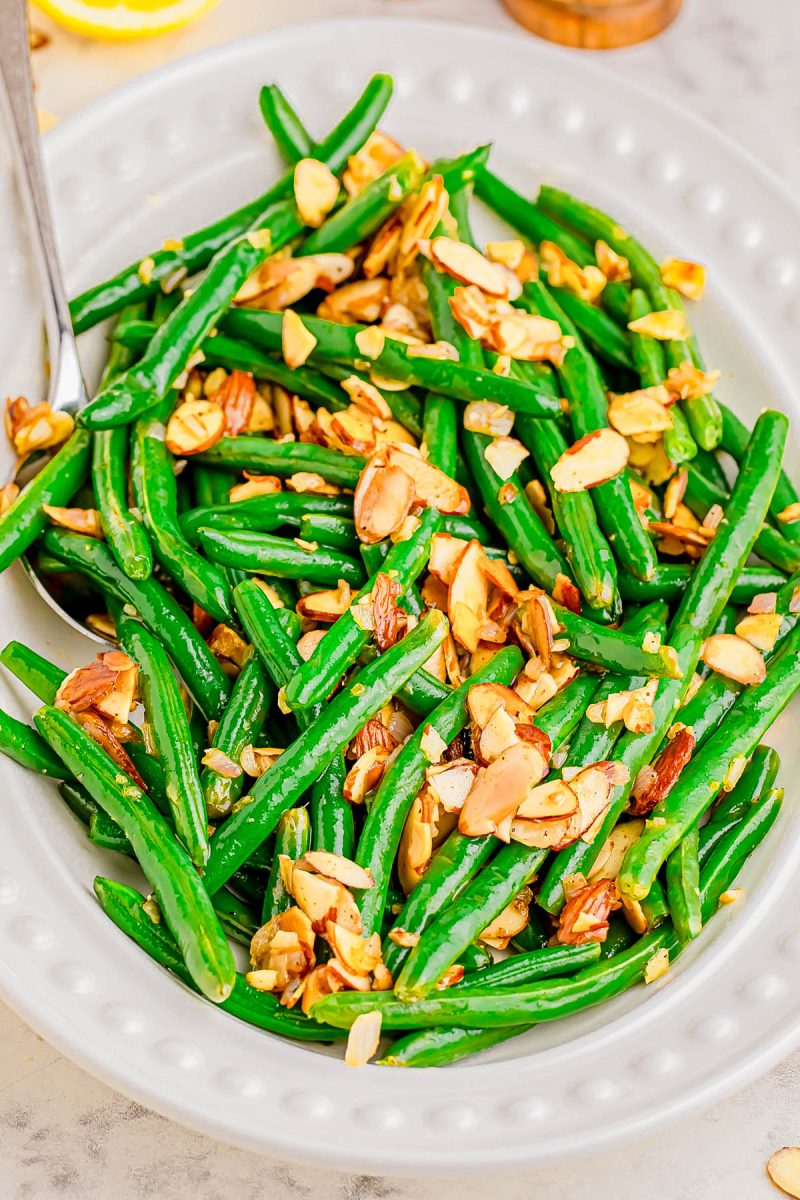 A white plate of cooked green beans topped with sliced toasted almonds.