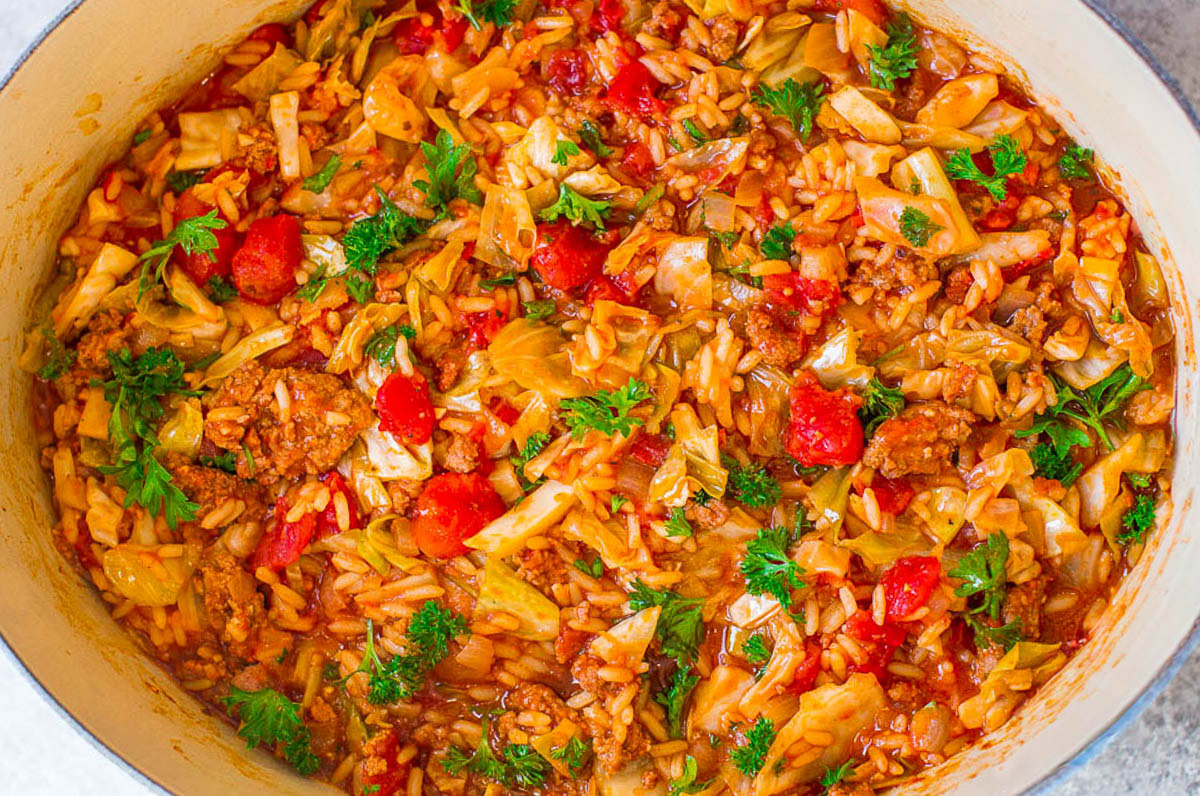 A pot of cooked cabbage, tomatoes, rice, and ground meat topped with fresh parsley.