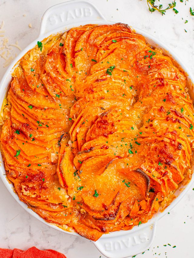 A baked sweet potato gratin in a round white dish, topped with melted cheese and garnished with chopped herbs.