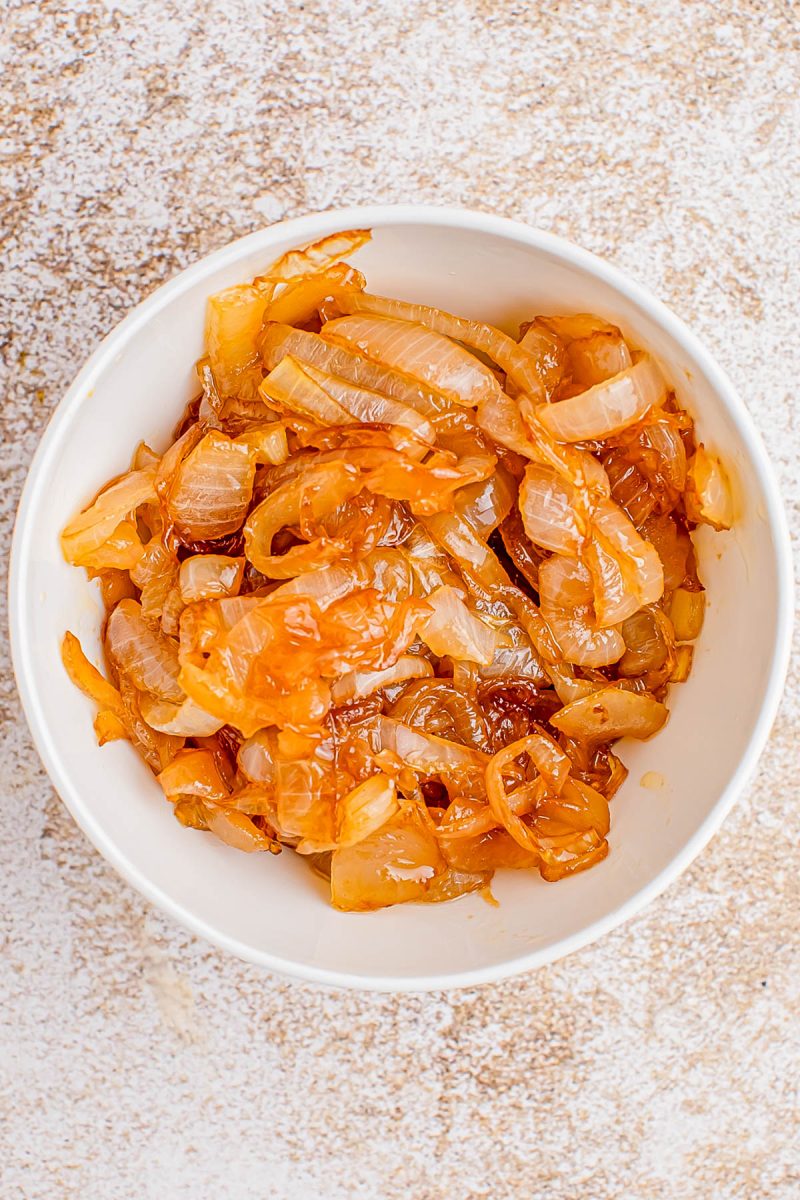 A white bowl filled with caramelized onions, placed on a light textured surface.