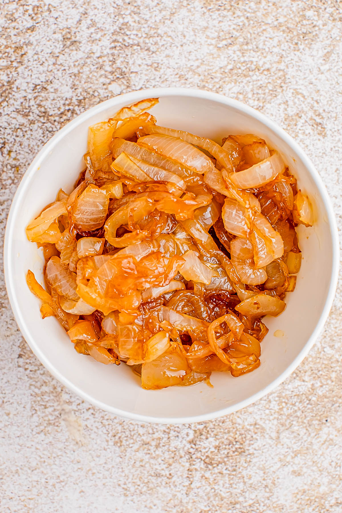 A white bowl filled with caramelized onions, placed on a light textured surface.