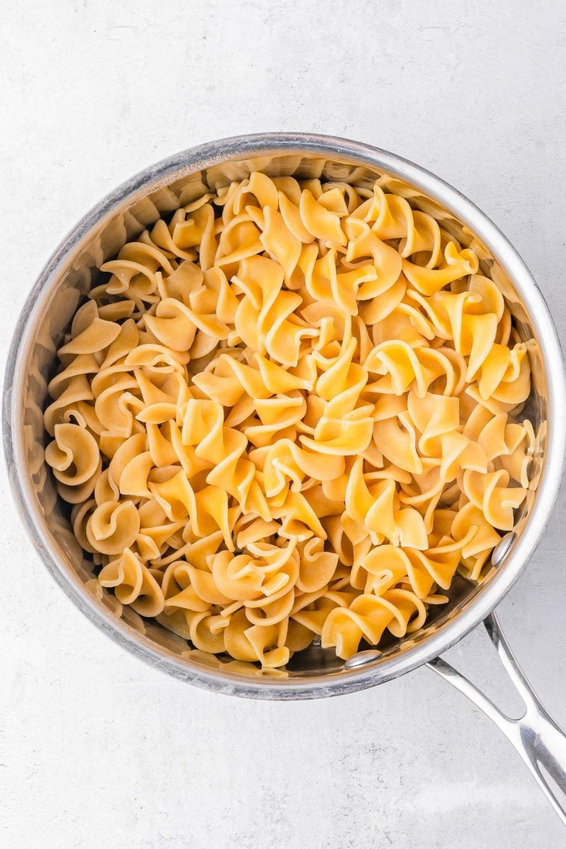 A stainless steel pot filled with cooked egg noodles on a white surface.