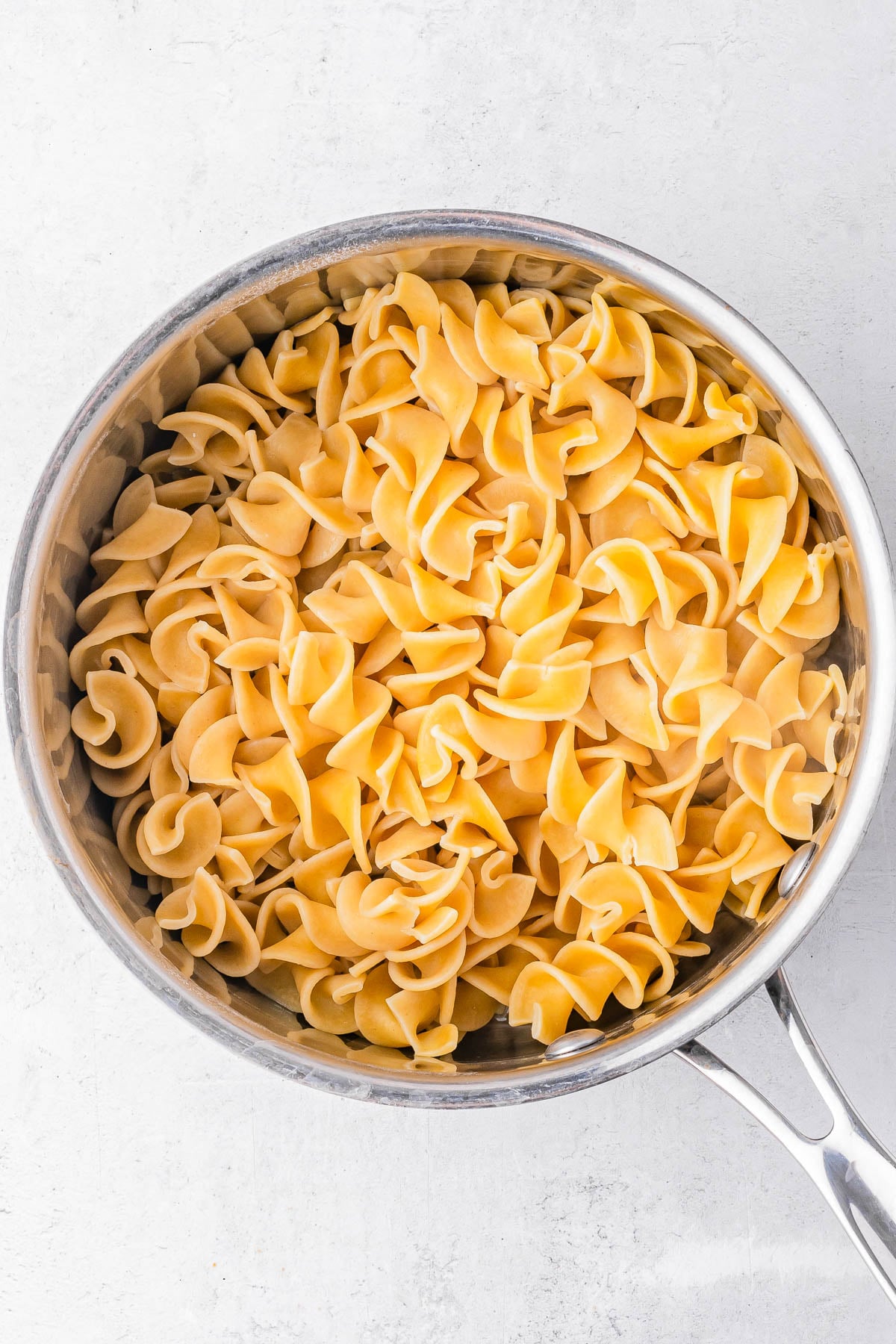 A stainless steel pot filled with cooked egg noodles on a white surface.