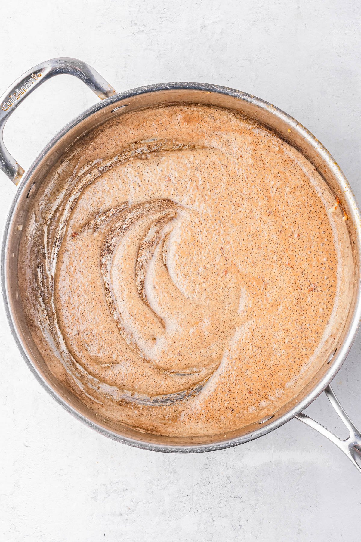 A large stainless steel pot filled with a light brown, frothy liquid sits on a light-colored surface.