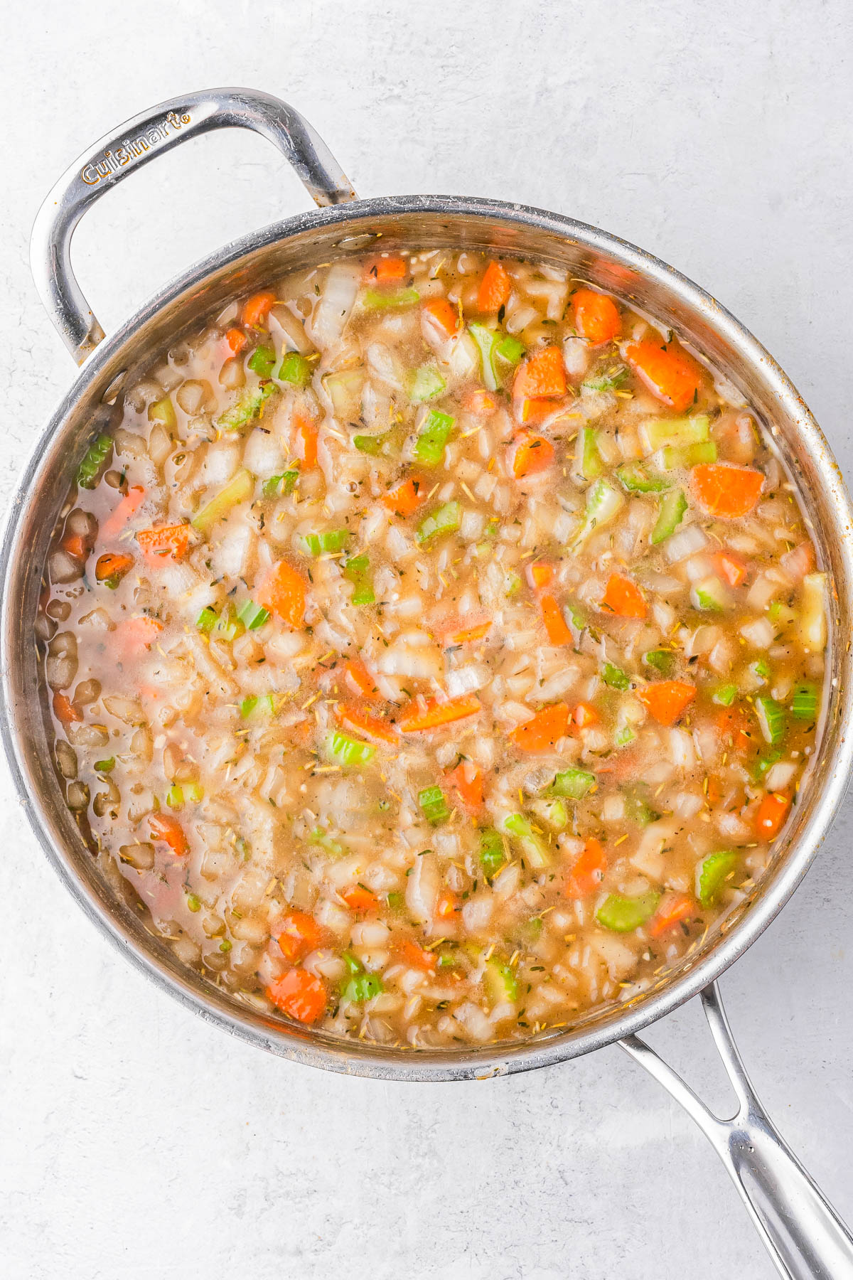 A stainless steel pot filled with a soup containing chopped carrots, celery, onions, and lentils in broth, shown from above.