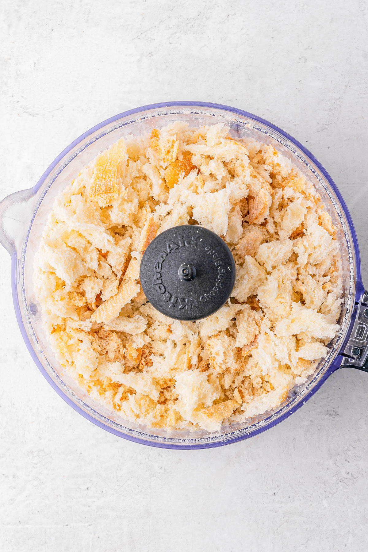 A food processor filled with freshly made white bread crumbs on a light countertop.