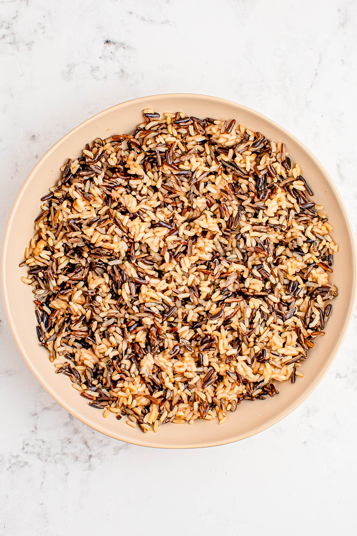 A bowl filled with a mixture of cooked wild rice and brown rice on a white marble surface.
