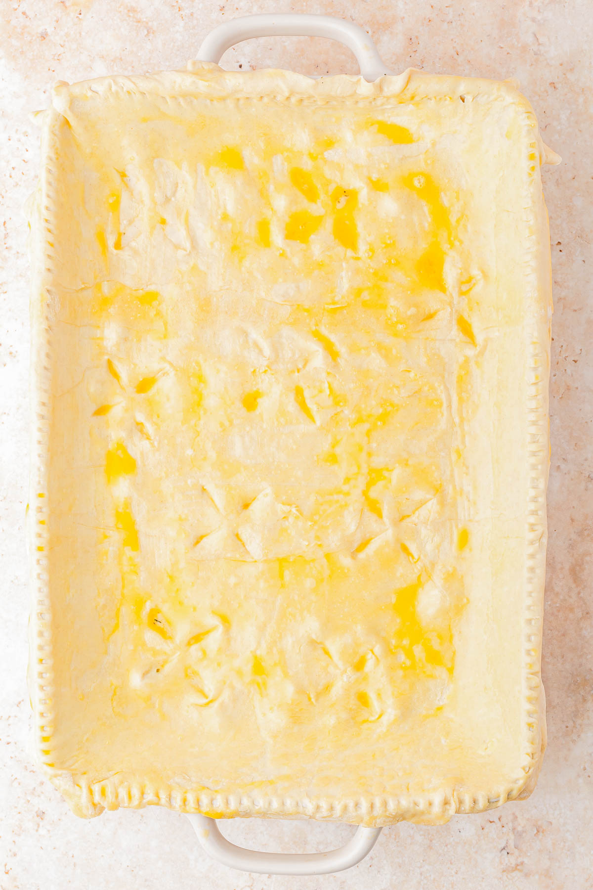 A rectangular baking dish lined with unbaked pie crust, edges crimped, and surface brushed with egg wash.