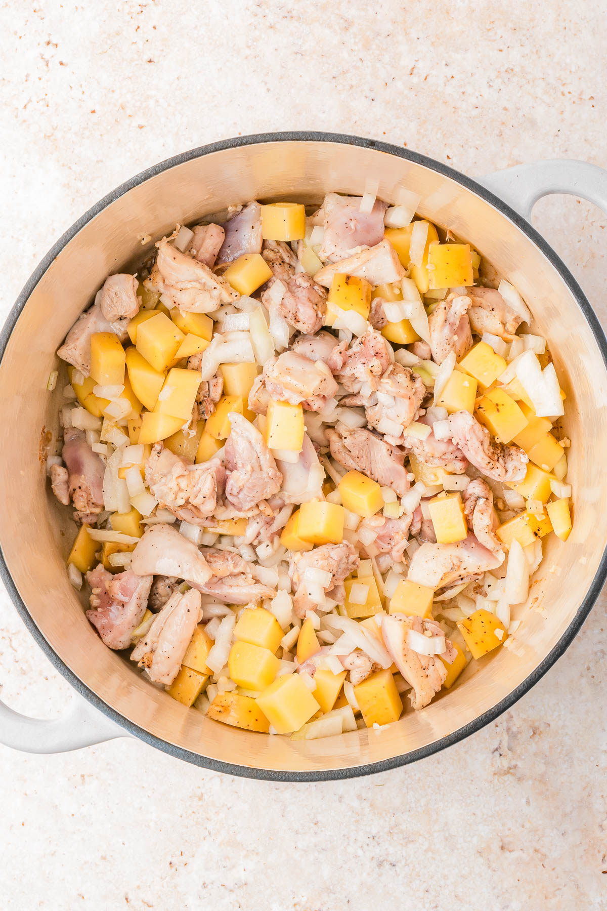 A pot filled with chopped raw chicken, yellow potatoes, and diced onions, seasoned and ready to cook.
