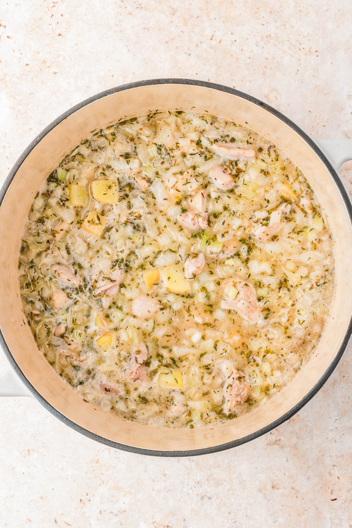 A large pot filled with a mixture of chopped chicken, potatoes, herbs, and onions simmering in broth.