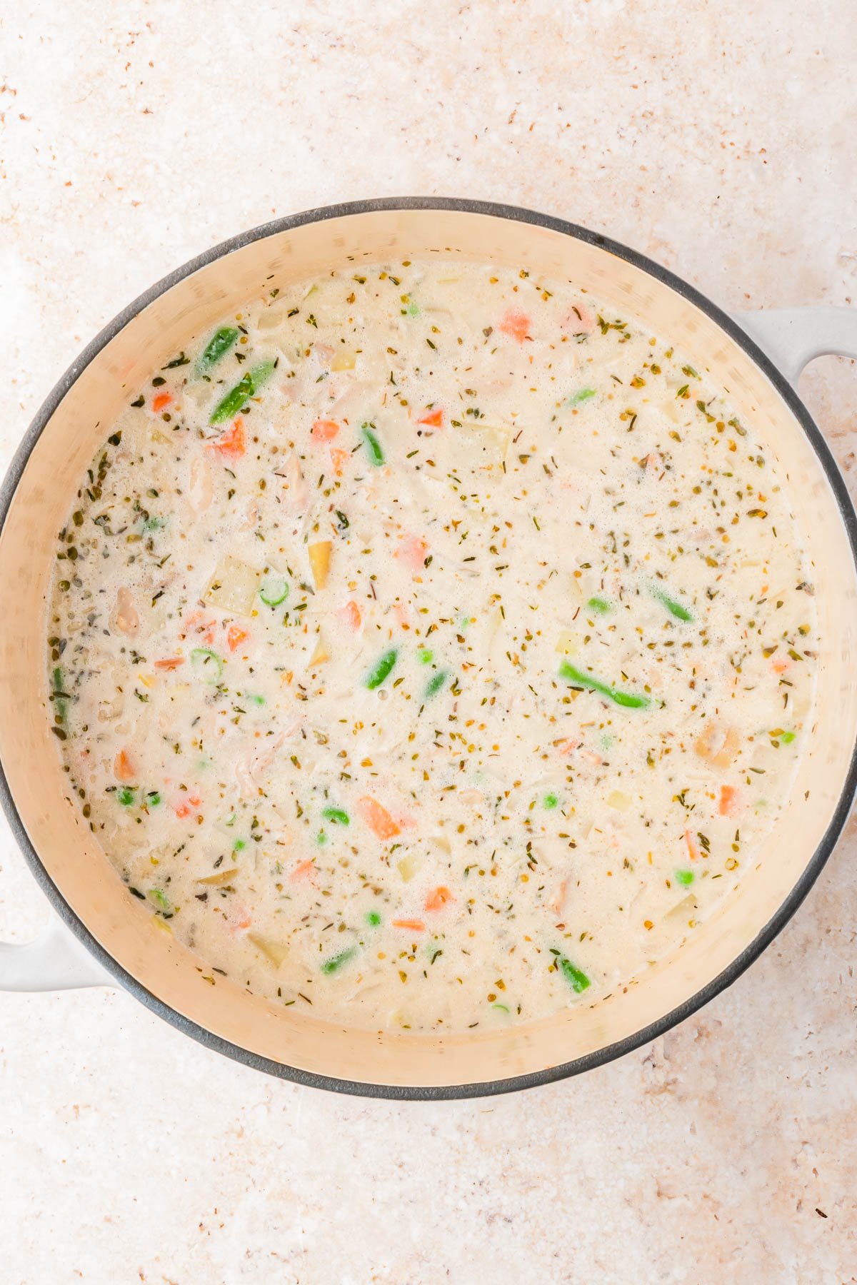 A large pot filled with creamy vegetable soup, containing visible pieces of carrots, green beans, and herbs.