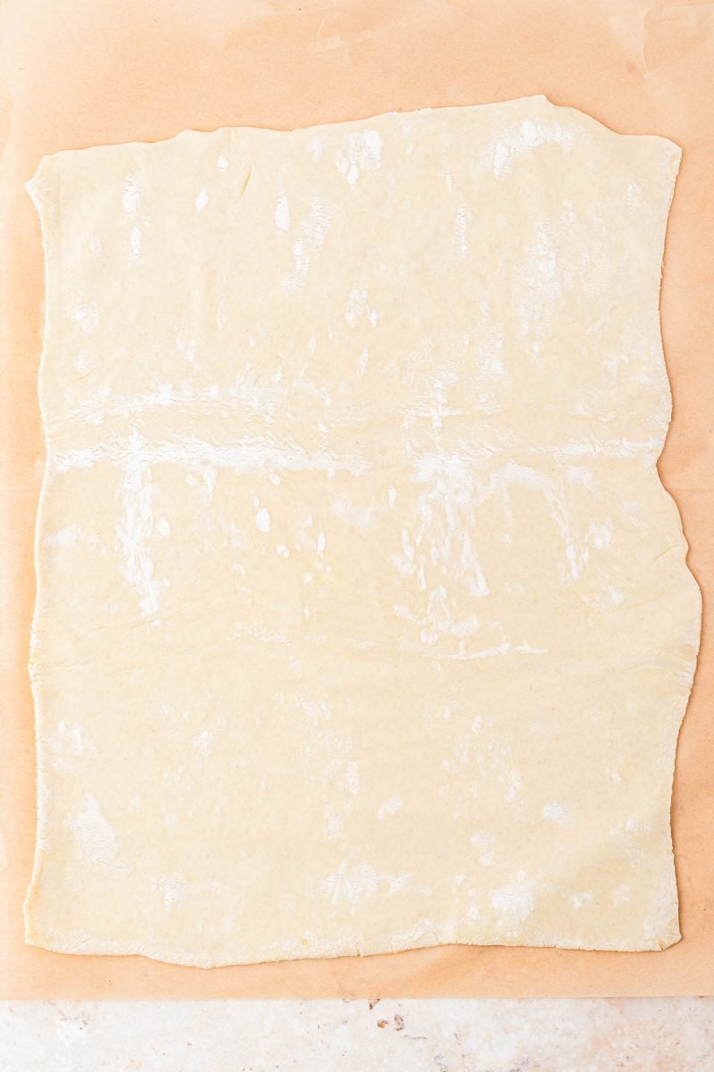 A sheet of raw, rolled-out dough on a piece of parchment paper.