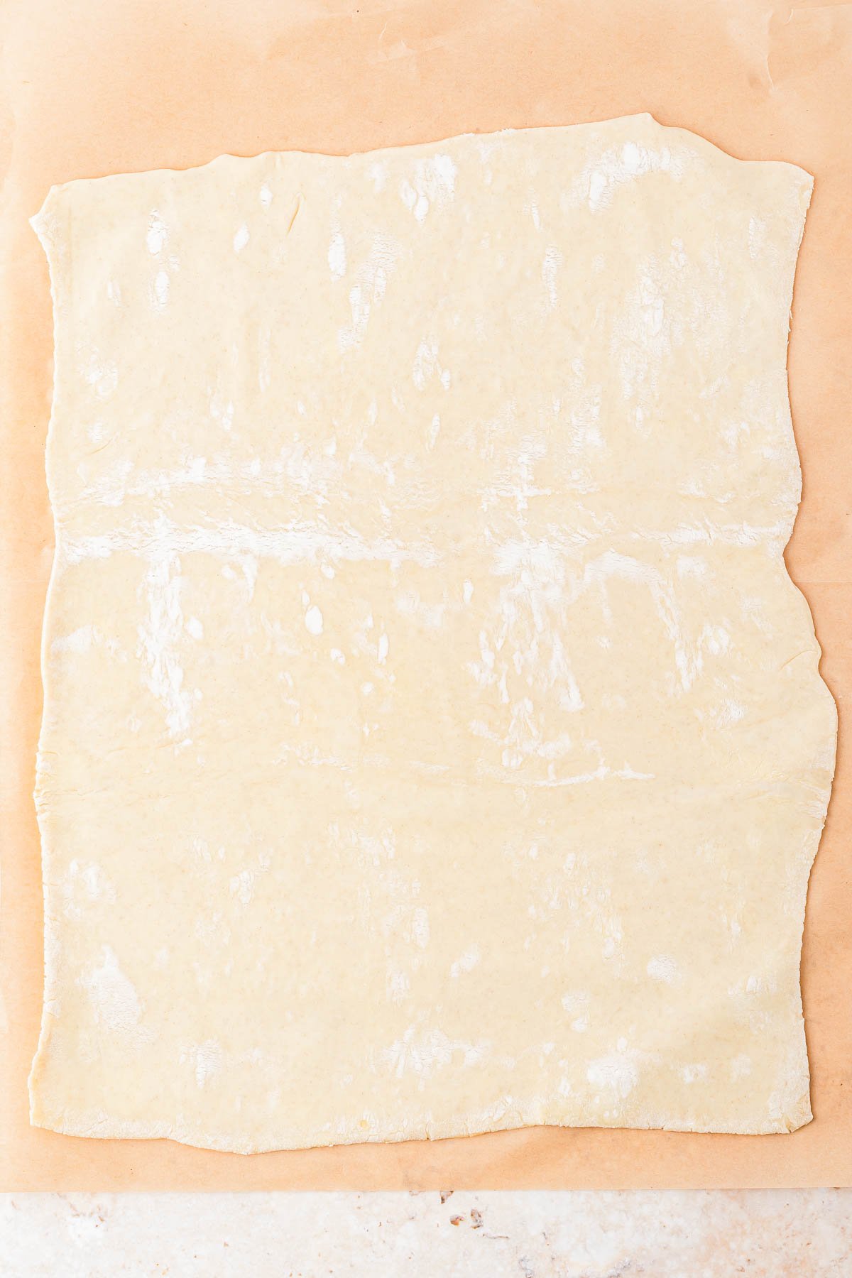 A sheet of raw, rolled-out dough on a piece of parchment paper.