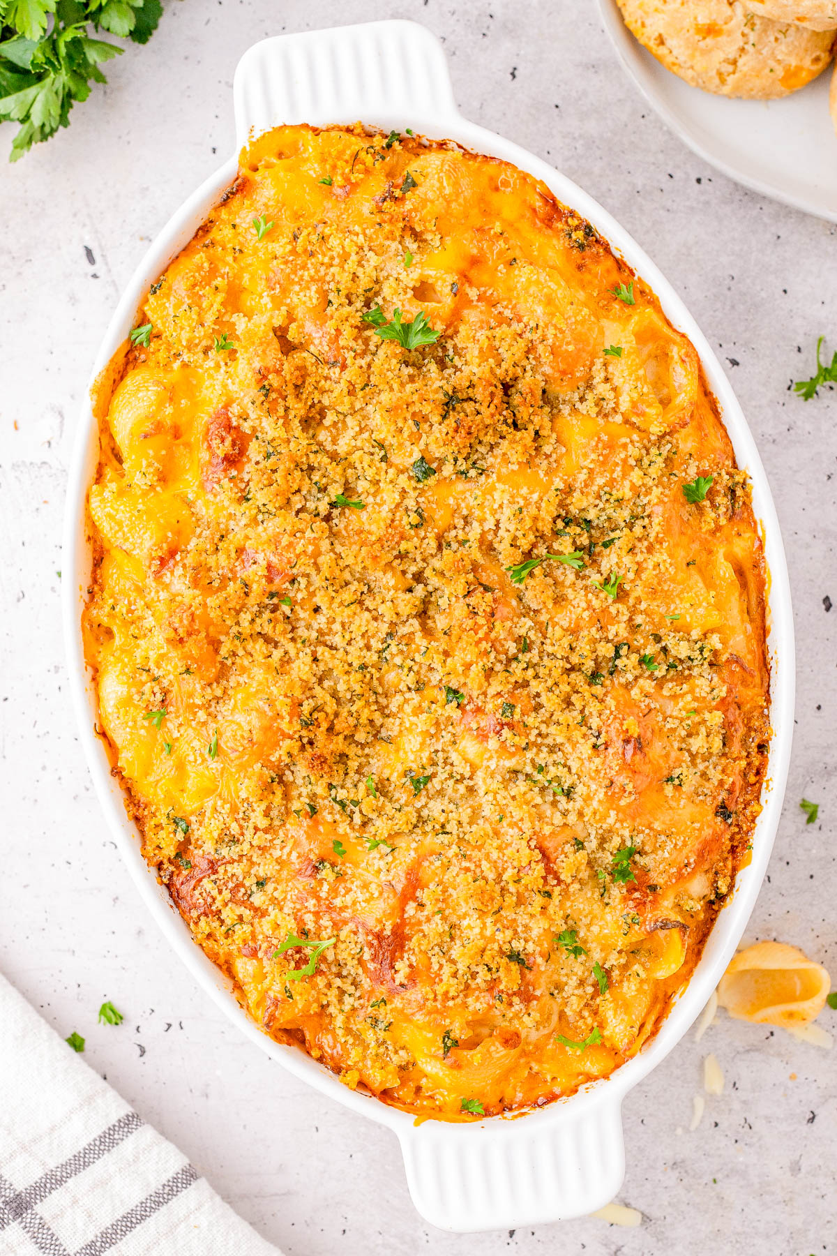 A baked macaroni and cheese casserole with a golden breadcrumb topping in a white oval dish, garnished with chopped herbs.