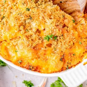 Baked macaroni and cheese topped with golden breadcrumbs and garnished with parsley in a white dish, with a wooden spoon scooping a portion.