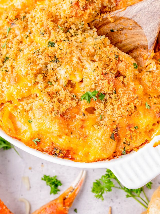 Baked macaroni and cheese topped with golden breadcrumbs and garnished with parsley in a white dish, with a wooden spoon scooping a portion.