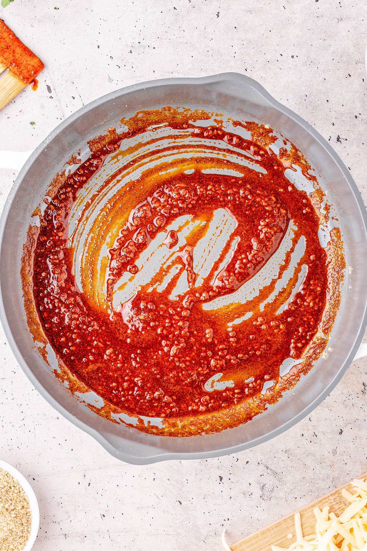 A gray pan containing a thin layer of cooked, red chorizo grease and meat bits on a light countertop.