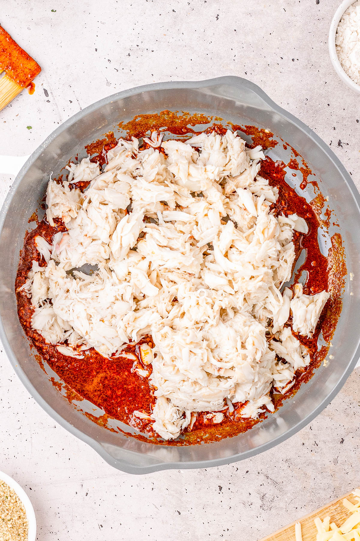 A large bowl containing lump crab meat on top of a mixture of reddish spices and sauce, placed on a light countertop.