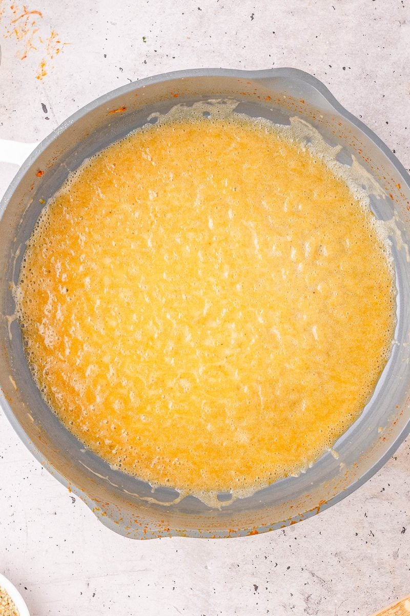 Overhead view of a pot filled with a yellow, bubbling liquid mixture, possibly in the process of being cooked or reduced.