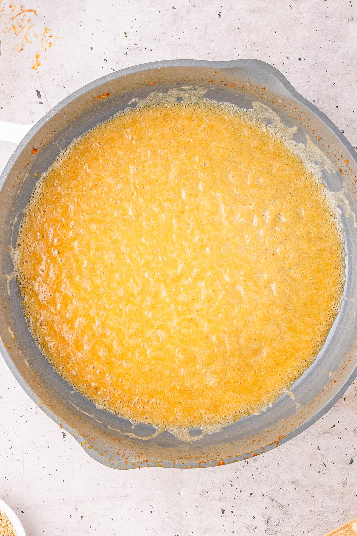 Overhead view of a pot filled with a yellow, bubbling liquid mixture, possibly in the process of being cooked or reduced.