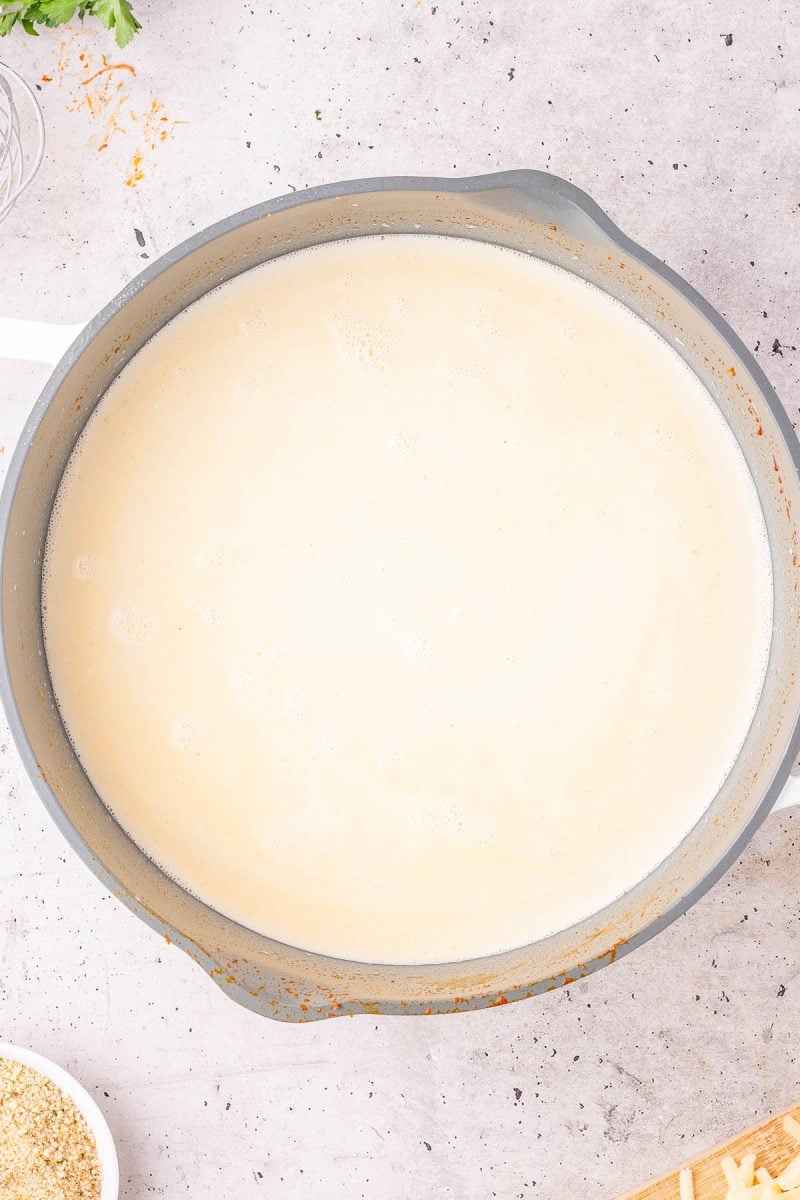 A large pot filled with creamy white sauce sits on a light-colored countertop.