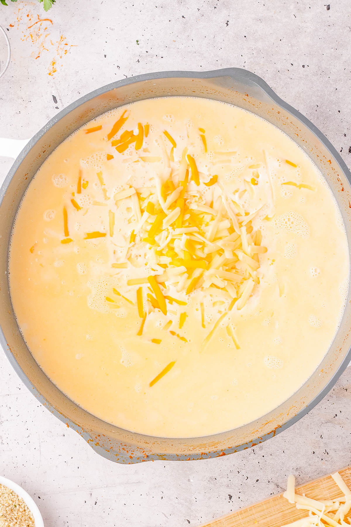 A gray pan filled with creamy yellow sauce topped with shredded cheese, sitting on a speckled countertop.